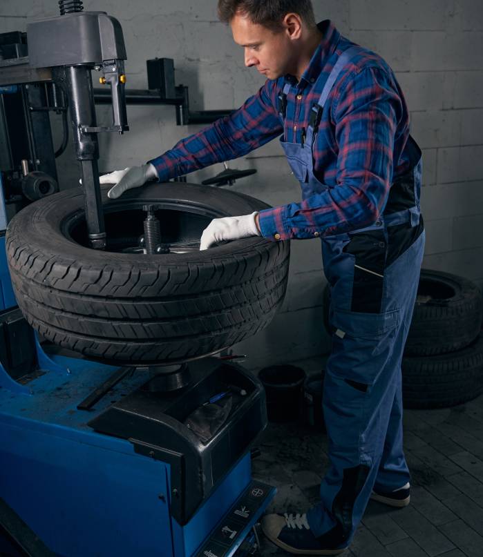 Employer in protective uniform and gloves standing near wheel and checking condition, performing repair